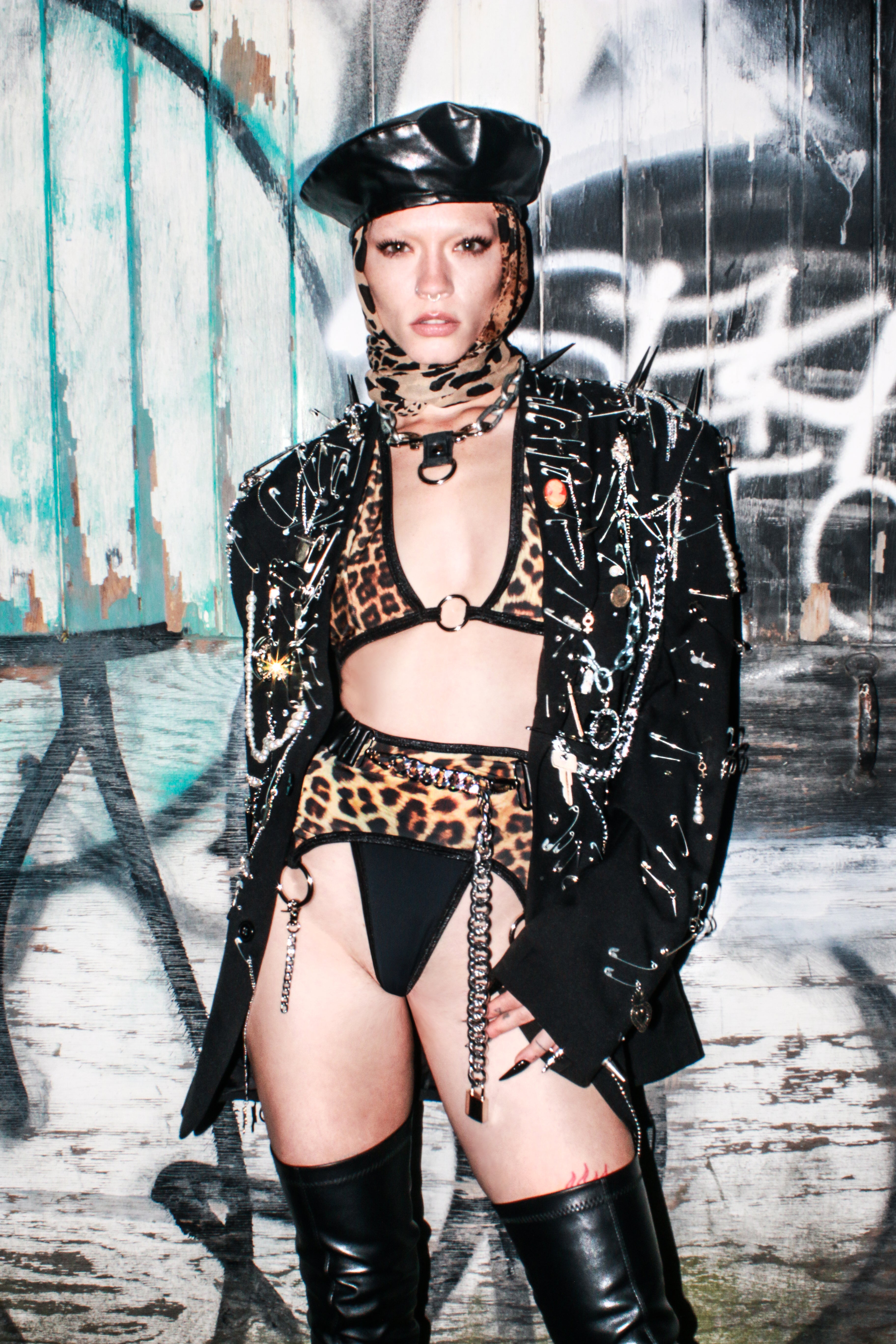 Person wearing a leopard print outfit with a black leather jacket against a graffiti-covered wall.